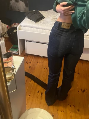 Mörkblå bootcut jeans från NA-KD - Säljer ett par mörkblå bootcut jeans från NA-KD med klassisk femficksdesign och hög midja. Jeansen har en snygg, figurnära passform upptill och släpper ut vid benen. Perfekta till sneakers eller boots och tillverkade i ett stretchigt denimtyg.