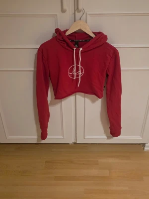 Röd cropped hoodie - Snygg röd cropped hoodie med vitt tryck på bröstet och vita dragsnören i huvan.