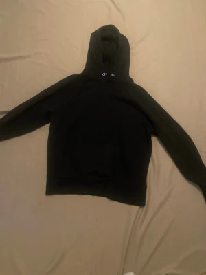Svart hoodie från H&M Basic XS - En enkel svart hoodie från H&M Basic i storlek XS. Hoodien har en klassisk huva med dragsko och en stor magficka framtill. Tillverkad i mjukt material som passar perfekt för en avslappnad stil. Perfekt att slänga på sig när det är lite kyligt ute.