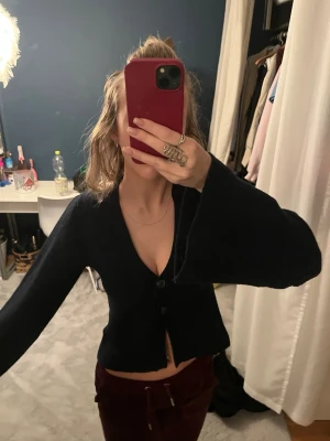 Marinblå  croppad kofta med vida ärmar - Snygg marinblå  kofta med croppad passform och vida ärmar. Koftan har v-ringning och knäpps med två knappar framtill. Perfekt för att lyfta en enkel outfit och passar till både jeans och kjol.