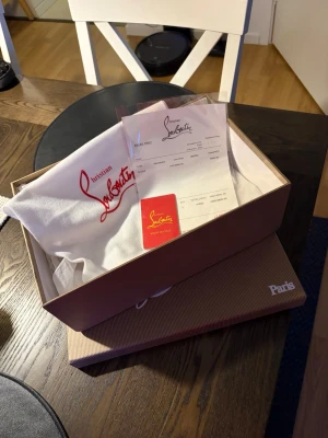 Christian Louboutin svarta sneakers - Svarta sneakers från Christian Louboutin i mocka med ikoniska röda sulor och svarta nitar på tån. Klassisk låg modell med snörning och exklusiv känsla. Kommer med originalkartong och dustbag. Saknar en del spikar som syns på bild