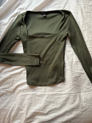 Olivgrön långärmad topp från Amisu - Snygg olivgrön topp från Amisu med lång ärm och fyrkantig urringning. Tillverkad i mjuk bomullsmix som sitter tight mot kroppen. Perfekt att styla med jeans eller kjol för en trendig look.