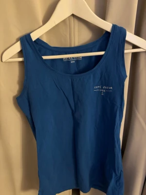 Blå linnetopp från Reaction - Snygg blå linnetopp från Reaction med tryck 'Côte d'Azur 1755' på bröstet. Toppen har rund halsringning och är ärmlös, Helt oanvänd men utan prislapp