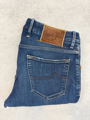 Blå raka jeans från Jacob Cohen - Snygga blå jeans från Jacob Cohen med raka ben och klassisk femficksmodell. Jeansen har en läderpatch med logga bak i midjan och kontrastsömmar. Tillverkade i slitstark denim med lätt tvättade detaljer för en avslappnad look.