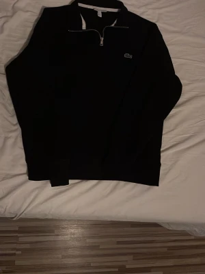 Svart halvzip tröja från Lacoste - Snygg svart tröja från Lacoste med halv dragkedja och klassisk krokodillogo på bröstet. Tröjan har lång ärm och en stilren design som passar perfekt till jeans eller chinos. Materialet känns mjukt och bekvämt.