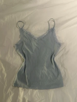 Ljusblå ribbad linnetopp med spets -  ljusblå linnetopp med tunna axelband och spetsdetaljer längs v ringningen. 