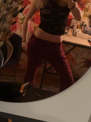 Röda leopardmönstrade jeans - Säljer ett par röda jeans med leopardmönster. Modellen har raka ben och klassisk femficksdesign. Jeansen har knappgylf och är tillverkade i ett stretchigt material för extra komfort. Perfekta för dig som vill sticka ut med en cool och trendig look.