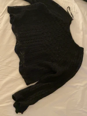 Svart stickad croppad tröja - Svart stickad tröja med croppad passform och lång ärm. Tröjan har ett genombrutet mönster som ger en cool och trendig look. Perfekt att styla över ett linne eller topp. Mjukt material och avslappnad passform.