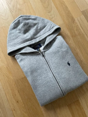 Grå hoodie från Polo Ralph Lauren, strl 14/16 år - Snygg grå hoodie från Polo Ralph Lauren. Hoodien är i bra skick och har inga skador. Nypris ca 1200 kr mitt pris endast 199 kr. Fraktar inom 1 dag, om du har någon fundering så är det bara att höra av sig😊