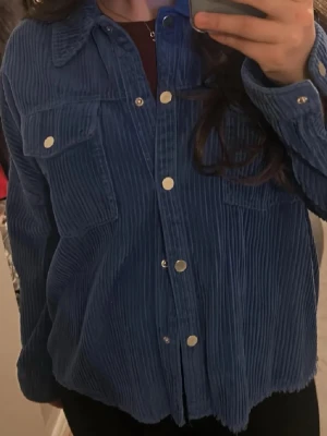 Blå Manchester från Zara - Snygg blå overshirt från Zara i manchestertyg med tryckknappar framtill och två bröstfickor. Skjortan har en avslappnad passform och klassisk krage, perfekt att slänga över en t-shirt för en cool look.