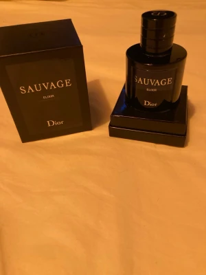 Dior Sauvage Elixir parfym - En exklusiv herrparfym i en elegant, mörkblå glasflaska med silverdetaljer. Flaskan har en rund form och kommer i en lyxig svart förpackning med tydlig logga. Doften är intensiv och maskulin, perfekt för dig som vill sticka ut. Iprincip helt ny har använts max 5 sprej.