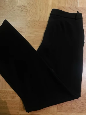 Svarta kostymbyxor med fickdetalj - Snygga svarta kostymbyxor med klassisk rak passform och diskret fickdetalj bak. Byxorna har bälteshällor och är tillverkade i ett slätt tyg som ger en stilren look. Perfekta för dig som vill ha en clean och tidlös stil. Passar mig som är strl s/m.
