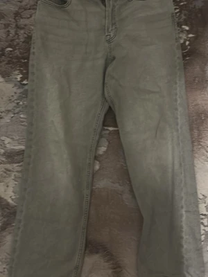 Grå raka jeans från Jack & Jones - Säljer ett par grå jeans från Jack & Jones med rak passform och klassisk femficksdesign. Jeansen har bälteshällor, knappgylf och är tillverkade i ett slitstarkt denimtyg. Perfekta för en avslappnad och stilren look.