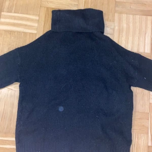 Svart polotröja i stickat material - Mysig svart stickad polotröja med lång ärm och ribbade muddar. Perfekt för lager-på-lager och enkel att matcha med olika outfits. Hög polokrage som ger extra värme och stil.