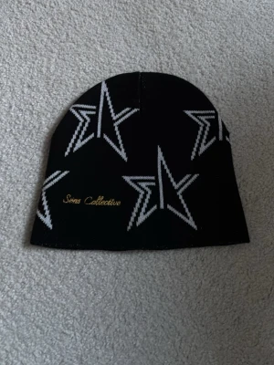 Svart mössa med stjärnor Sens Collective - Säljer en svart mössa från Sens Collective med vita stjärnmönster och guldfärgad logga broderad på sidan. Mössan är designad i Sverige och tillverkad i Portugal. Perfekt accessoar för dig som vill sticka ut med en cool och unik stil.