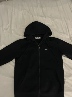 Svart hoodie från Comme des Garçons Play S/SX - Säljer en svart hoodie med dragkedja från Comme des Garçons. Hoodien har fickor fram och snörning i huvan.