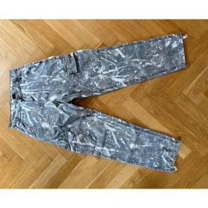 Grå/gröna  cargobyxor - Säljer ett par grå cargobyxor med vitt splattermönster och raka ben. Byxorna har flera praktiska fickor på sidorna och klassisk cargomodell. Perfekta för en streetwear-look och riktigt snygga till sneakers.