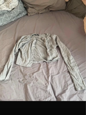 Grå cropped kofta  - Säljer en ljusgrå cropped kofta med långa ärmar och knäppning framtill. Koftan är tunn och har en enkel, stilren design som passar perfekt till lager-på-lager outfits.