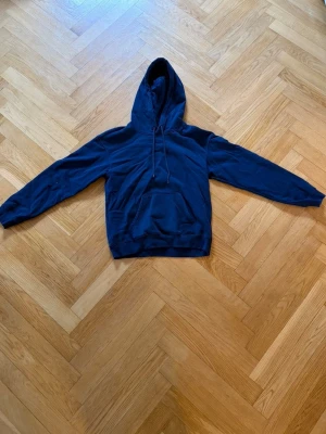 Mörkblå hoodie med ficka - En stilren mörkblå hoodie med huva och dragsnören. Klassisk känguruficka framtill och ribbade muddar vid ärmslut och nederkant. Perfekt för en avslappnad look. Materialet känns mjukt och bekvämt.