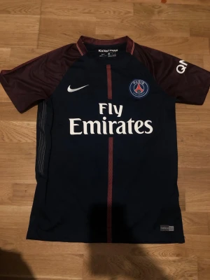 PSG Neymar Jr matchtröja Nike - Mörkblå och vinröd PSG matchtröja från Nike med Neymar Jr och nummer 10 på ryggen. Tröjan har klubbmärke, sponsorloggor och vita detaljer. Perfekt för fotbollsfans som vill visa sitt stöd för Paris Saint-Germain.
