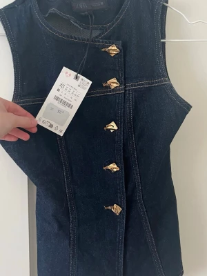 Mörkblå ärmlös jeansblus från Zara - Snygg mörkblå ärmlös jeansblus från Zara med markerade sömmar och guldiga knappar framtill. Toppen har en figurnära passform och är tillverkad i denim med coola detaljer. Perfekt att styla med både kjol och byxor. För liten för mig vill gärna byta med någon som har i storlek S🩷🩷