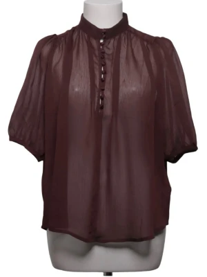 Brun transparent blus med knappar h&m - Snygg brun transparent blus med korta puffärmar och dekorativa knappar framtill. Blusen har en hög krage och är tillverkad i ett lätt, luftigt material som ger en elegant look. Perfekt att styla med linne under för en trendig outfit.