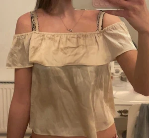 Beige offshoulder blus med volang - Söt beige offshoulder blus med volang runt axlarna. Luftig och lätt modell som ger en avslappnad vibe. Perfekt till sommaren och enkel att styla med både jeans och kjol.
