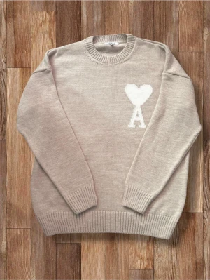 Beige tröja Ami Paris - Snygg beige stickad tröja från Ami Paris med rund halsringning och ribbade muddar. På bröstet finns ett vitt hjärta och bokstaven 'A' som ger en unik touch. Perfekt för dig som gillar stilrena plagg med en twist.