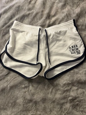 Vita shorts från Abercrombie med snörning - Snygga vita shorts från Abercrombie med marinblå detaljer och snörning i midjan. Broderad logga på ena benet och mjukt bomullsmaterial. Perfekta för sommaren och chill dagar.