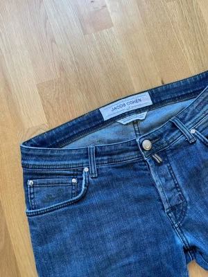 Blå jeans från Jacob Cohën - Snygga blå jeans från Jacob Cohën med klassisk femficksmodell och raka ben. Jeansen har en medelhög midja och subtila slitningar för en cool look. Tillverkade i mjuk denim med stretch för extra komfort.
