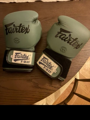 Fairtex gröna boxningshandskar - Säljer ett par gröna boxningshandskar från Fairtex, modell F-DAY. Handskarna har bred kardborreknäppning och är tillverkade i slitstarkt läder. Perfekta för träning inom boxning eller thaiboxning.