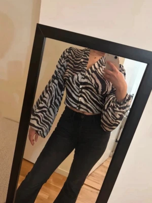 Zebramönstrad croppad blus  - Snygg croppad blus från Miss Selfridge med zebramönster i svart och vitt. Blusen har vida, långa ärmar och v-ringad hals. Perfekt för dig som vill sticka ut med ett djurmönster och trendig passform.