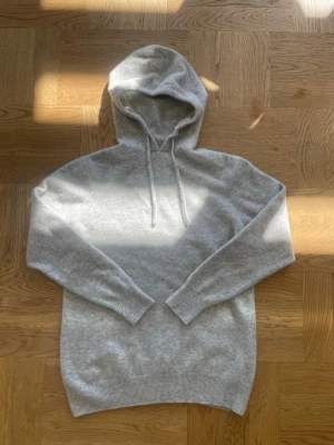 Ljusgrå merinoull hoodie  - Säljer en stilren ljusgrå merinoull hoodie med huva och dragsnören. Hoodien har långa ärmar och ribbade muddar vid ärmslut och nederkant. Perfekt för en avslappnad look och supermjuk att ha på sig.
