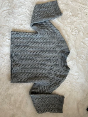 Grå kabelstickad tröja från Lindex - Snygg grå kabelstickad tröja från Lindex med rund hals och ribbade muddar. Tröjan har ett klassiskt flätmönster och är perfekt för lager-på-lager-stil. Tillverkad i mjukt material som känns skönt mot huden. Använd några gånger, pris kan diskuteras. 