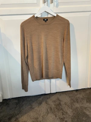 Beige stickad tröja från Uniqlo - En stilren beige stickad tröja från Uniqlo i tunt, mjukt material. Tröjan har rund halsringning, långa ärmar och ribbade muddar vid ärmslut och nederkant. Perfekt för lager på lager och enkel att matcha med olika outfits. 100% merinoull. Denna tröja har aldrig blivit använd. Bara legat i garderoben. Kvitto finns. Ställ gärna frågor☺️