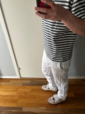 Vita linnebyxor med avslappnad passform - Säljer ett par vita linnebyxor med avslappnad och rak passform. Byxorna har resår i midjan och sidofickor, perfekta för en chill och stilren look. Tillverkade i lätt och luftigt linnematerial som passar perfekt till sommaren. Skriv gärna om du har funderingar🤍