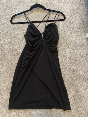 Svart slipklänning med tunna axelband - Svart klänning från Zara med tunna, korsade axelband som går att anpassa och rynkad detalj vid bysten. Klänningen har en slimmad passform och är gjord i ett mjukt, stretchigt material. Perfekt för dig som gillar en enkel och stilren look.