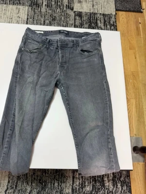 Grå jeans från Jack&Jones - Säljer ett par grå jeans från Jack&Jones med klassisk femficksdesign och raka ben. Jeansen har en snygg tvättad look och är tillverkade i bomull med lite stretch för extra komfort. Perfekt för dig som gillar en enkel och stilren stil.