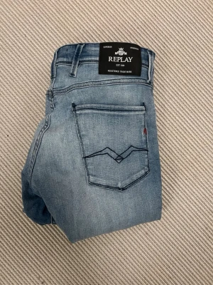 Ljusblå jeans från Replay - Snygga ljusblå jeans från Replay med klassisk femficksmodell och diskret tvättad look. Jeansen har raka ben och detaljerad bakficka med mörkblå söm. Perfekta för en avslappnad och trendig stil.