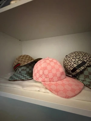 Rosa Gucci keps med GG-mönster - Säljer en snygg rosa keps från Gucci med det klassiska GG-monogrammet över hela kepsen. Kepsen har böjd skärm och justerbar rem bak. Tillverkad i canvasmaterial som ger en exklusiv känsla och passar perfekt till streetwear eller en trendig look.