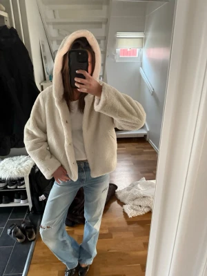 Beige teddyjacka med huva - Supermjuk teddyjacka i beige med stor huva och knäppning framtill. Jackan har en avslappnad passform och är gjord i fluffigt, fuskpälsliknande material som känns riktigt cozy. Perfekt för kyliga dagar när du vill vara både varm och snygg. Jackan är i storlek 164 men passar mig som vanligtvis har Xs/S.