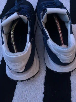 Philippe Model blå sneakers - Snygga sneakers från Philippe Model i marinblå mocka och textil med vita detaljer och vit sula. Klassisk låg modell med snörning och logga på hälen. Perfekta för en stilren och sportig look.