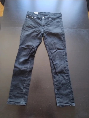 Svarta levi's  - Säljer ett par svarta jeans från Levis med klassisk modell och raka ben. Jeansen har normal passform och är tillverkade i bomull med en liten mängd stretch för extra komfort. Perfekta till din vardagsstil!