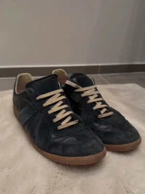 Maison Margiela Gats Navy - Maison Margiela sneakers i navy mocka och läder med vit snörning och gummisula. Klassisk låg modell med retrovibe och snygga detaljer. Perfekt för dig som gillar stilrena och tidlösa skor. Mycket bra skick självklart äkta men tyvärr ingen box 