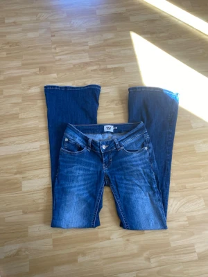 Blaze Lager 157 - Säljer ett par blå bootcut jeans från 157 med klassisk femficksdesign och snygga slitningar framtill. Jeansen har låg midja och vida ben, perfekt för en avslappnad och trendig look. Materialet är denim i bomull med lite stretch för extra komfort. Modellen Blaze. Storlek XS Short