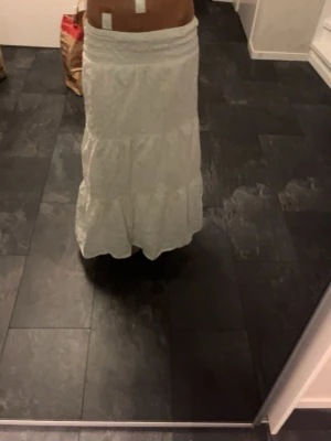 Vit långkjol med broderi från Gina Tricot - Säljer en vit långkjol från Gina Tricot med fina broderade detaljer och volanger. Kjolen har en elastisk midja och är perfekt för sommarens alla tillfällen. Superfin och luftig modell som ger en romantisk vibe.