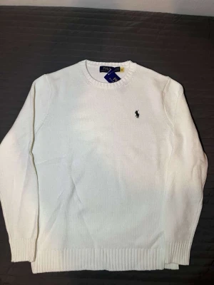 Vit stickad tröja från Polo Ralph Lauren - Klassisk vit stickad tröja från Polo Ralph Lauren med rund halsringning och diskret broderad logga på bröstet. Perfekt för dig som vill han en fin och vill se stilig tröja.