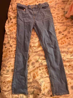Ljusblå skinny jeans med hög midja - Säljer ett par ljusblå skinny jeans med hög midja och klassisk femficksdesign. Jeansen har dragkedja och knapp framtill samt raka benslut. Perfekta för dig som gillar en tight passform och enkel stil.
