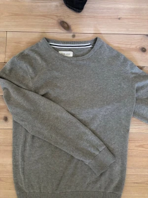 Grå  tröja  - En stilren grå tröja från Pier One med rund halsringning och ribbade muddar vid ärmslut och nederkant. Perfekt att matcha med jeans eller över en skjorta för en clean look. Materialet känns mjukt och bekvämt.