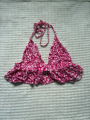 Rosa topp med volang och knyt - Säljer en rosa topp med vitt leopardmönster. Toppen har volangkant, knyt i nacken och omlottkänsla framtill. Perfekt för sommarens strandhäng och poolpartyn.